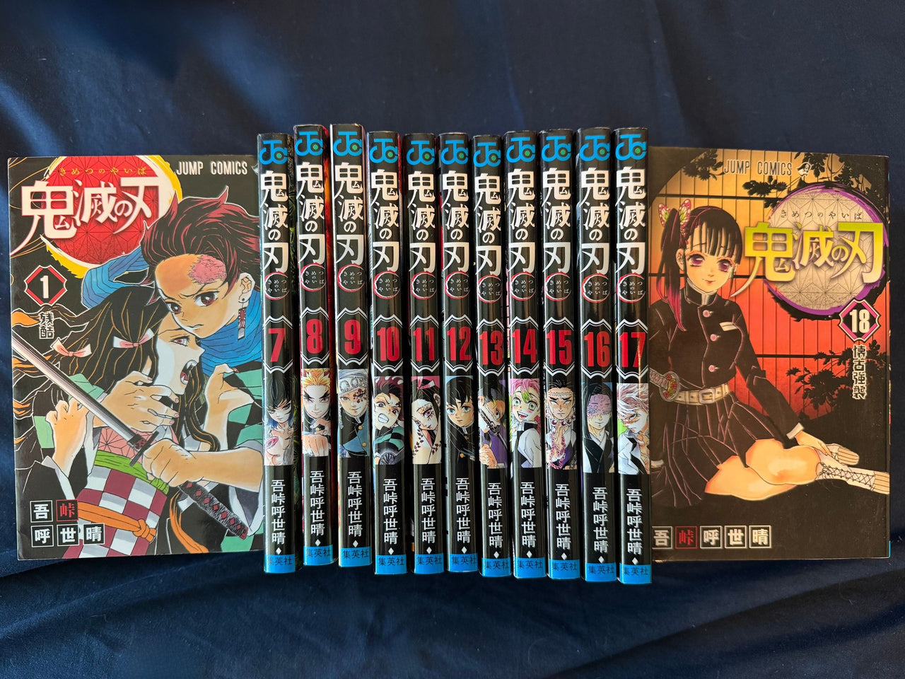 Demon Slayer volume 1 and volume 18 covers beside the numbered spines of volumes 7 to 17